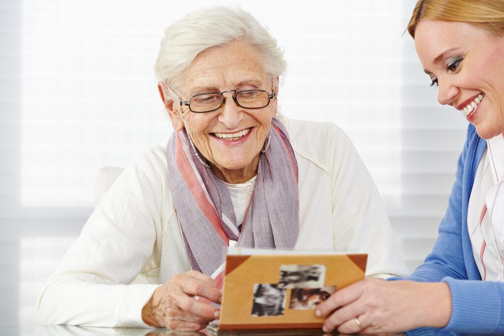 Happy senior woman watching photo album with eldercare nurse