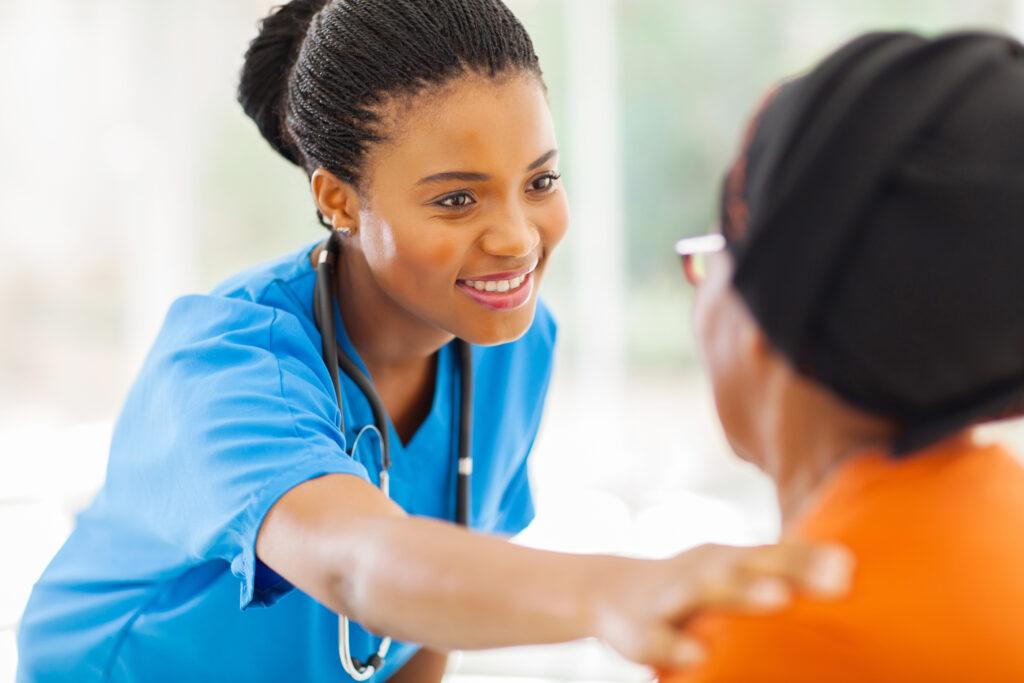 caring african medical nurse comforting senior patient in office